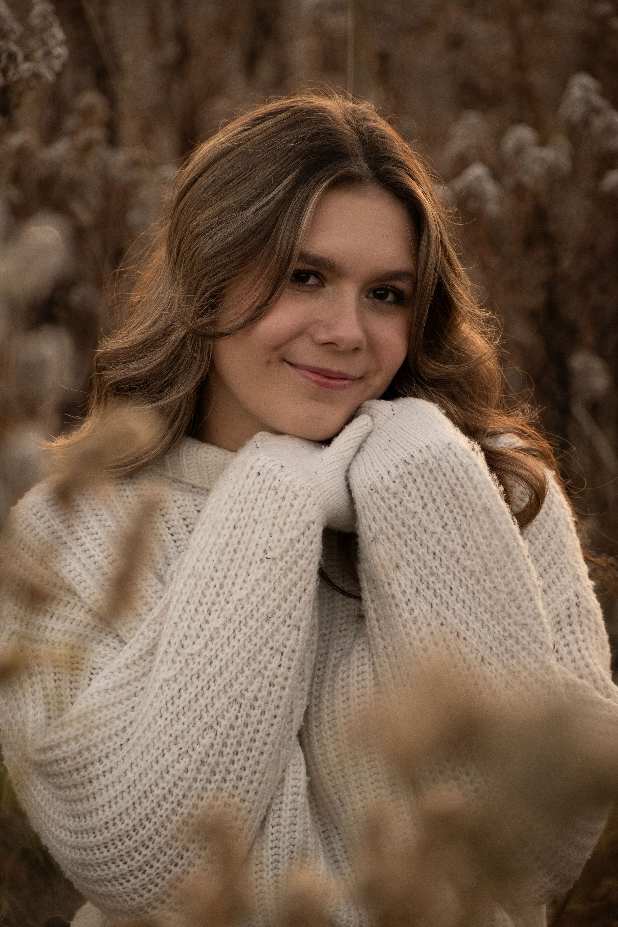 Person in cozy white knit sweater poses against natural brown background.