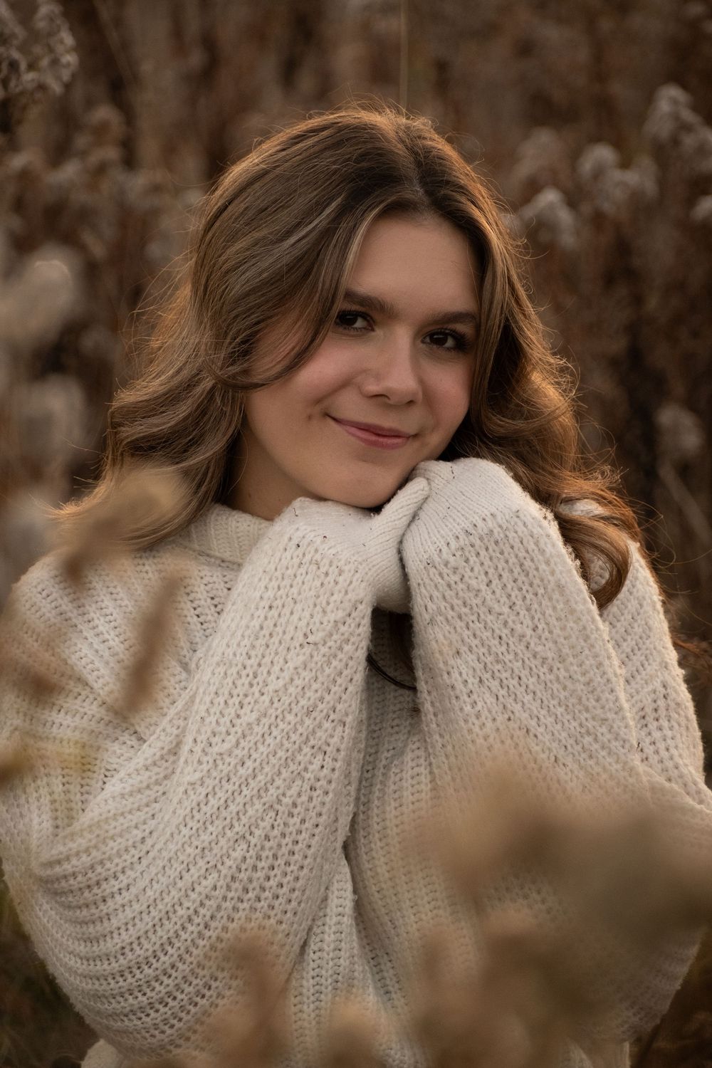 Person in cozy white knit sweater poses against natural brown background.