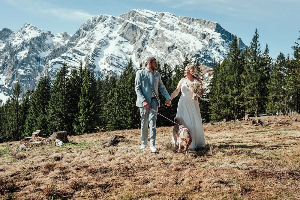 A scenic mountain elopement ceremony takes place on a rocky hillside with snow-capped peaks in the background.