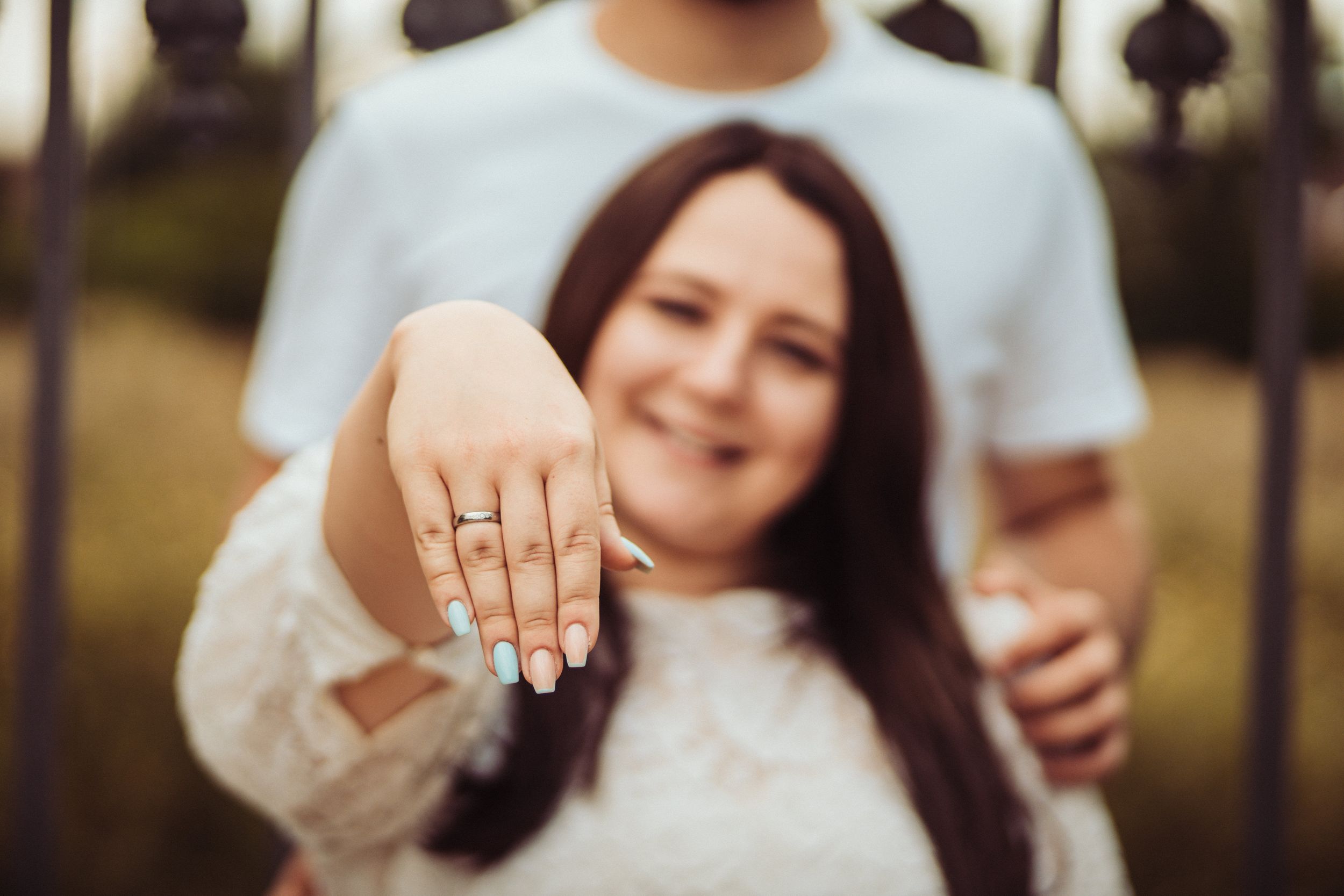 Close-up shot of hands showing off an engagement ring in an outdoor setting.