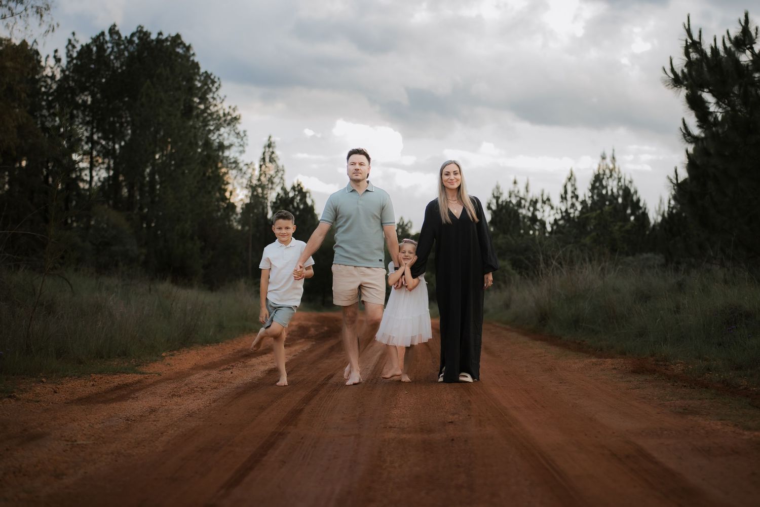 Family walking together on a rustic dirt road surrounded by trees and natural landscape during golden hour.