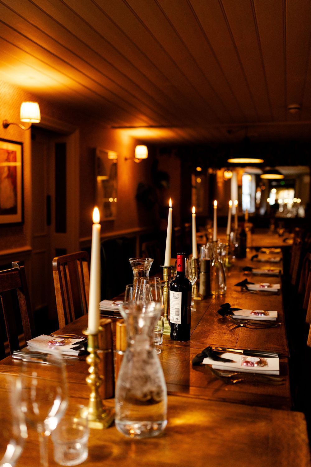 Elegant restaurant table setting with candlelight, wine glasses, and place settings on a long wooden table.