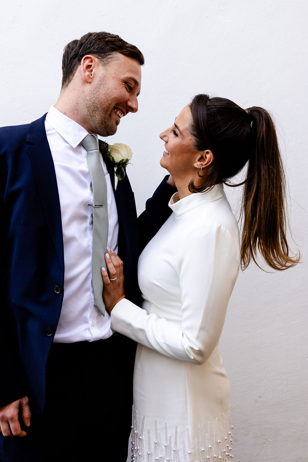 Romantic wedding couple in white and navy sharing intimate moments against a light background.