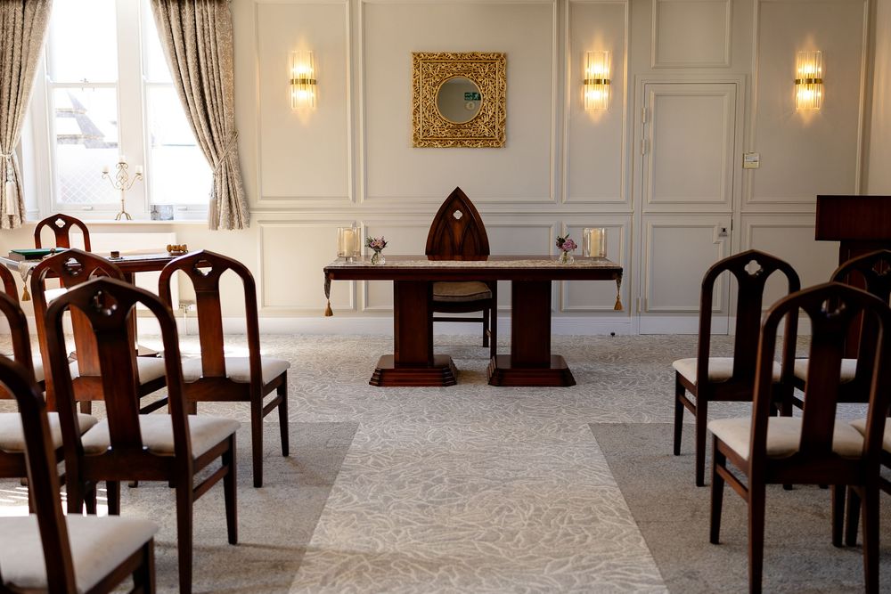 Interior of a marriage room with wooden chairs arranged in rows facing a podium in an elegant white-walled space.