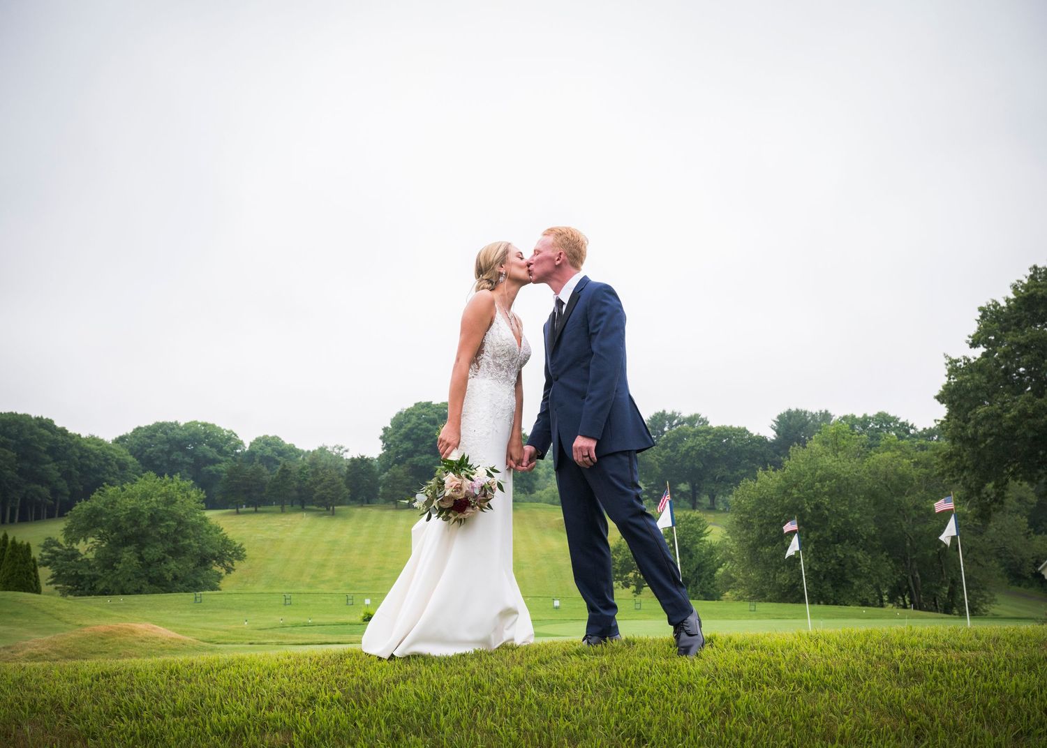 A couple in wedding attire shares a romantic moment on a lush green golf course.
