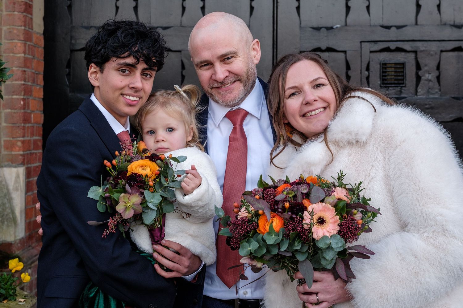 A group of wedding party members smile together while holding colorful autumn bouquets with orange and peach flowers.