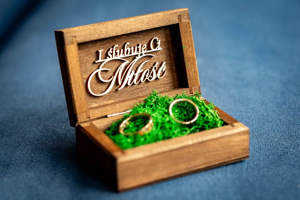 Rustic wooden ring box with green moss interior displayed on blue background.