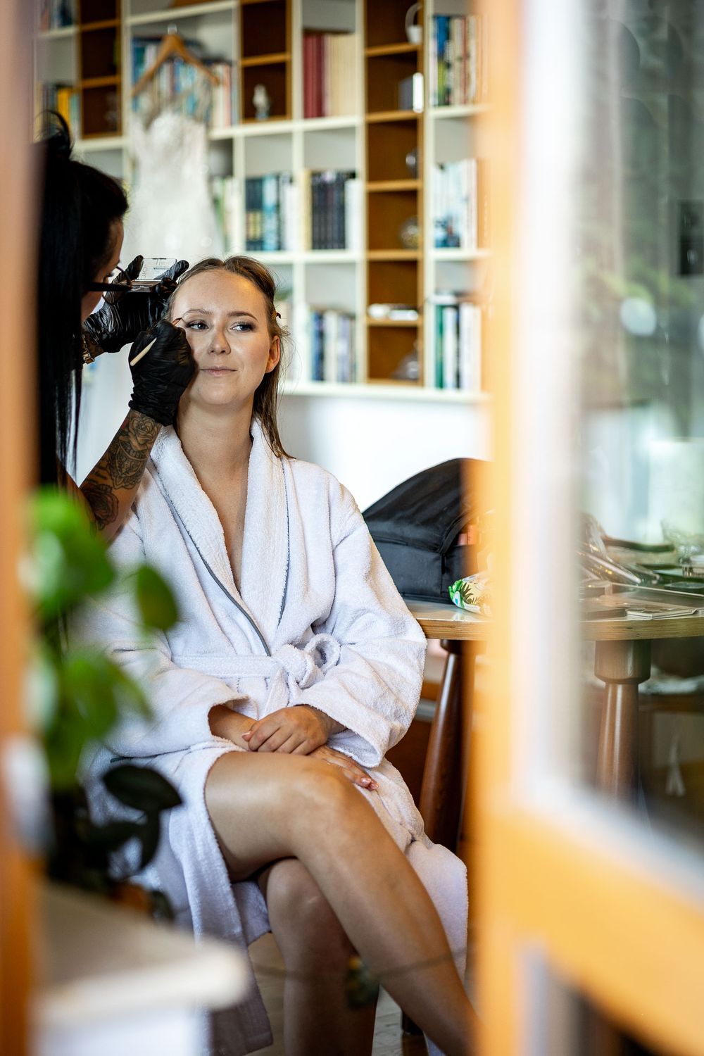 Relaxed moment in white robe by window during wedding morning preparations.