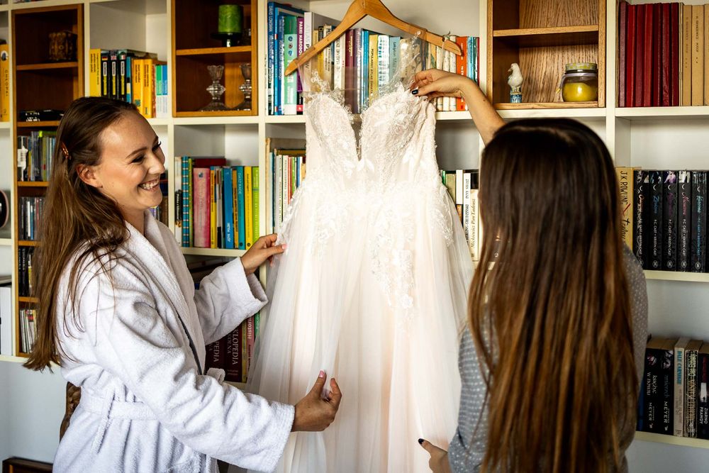 Wedding dress displayed on hanger in room with bookshelves.