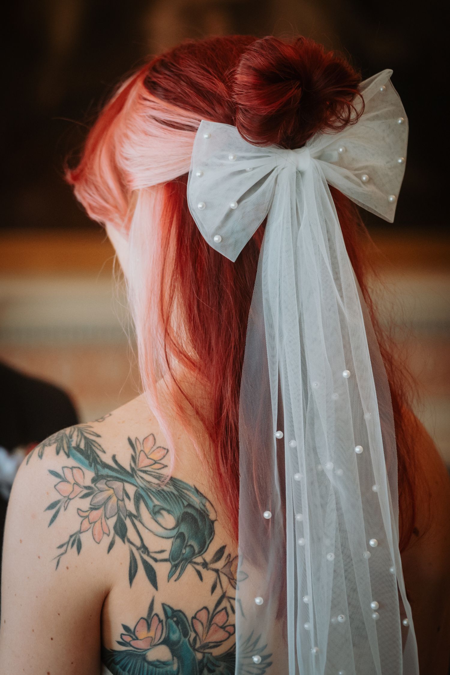 A delicate white bow veil adorns pink hair next to a floral shoulder tattoo in elegant bridal detail shots.