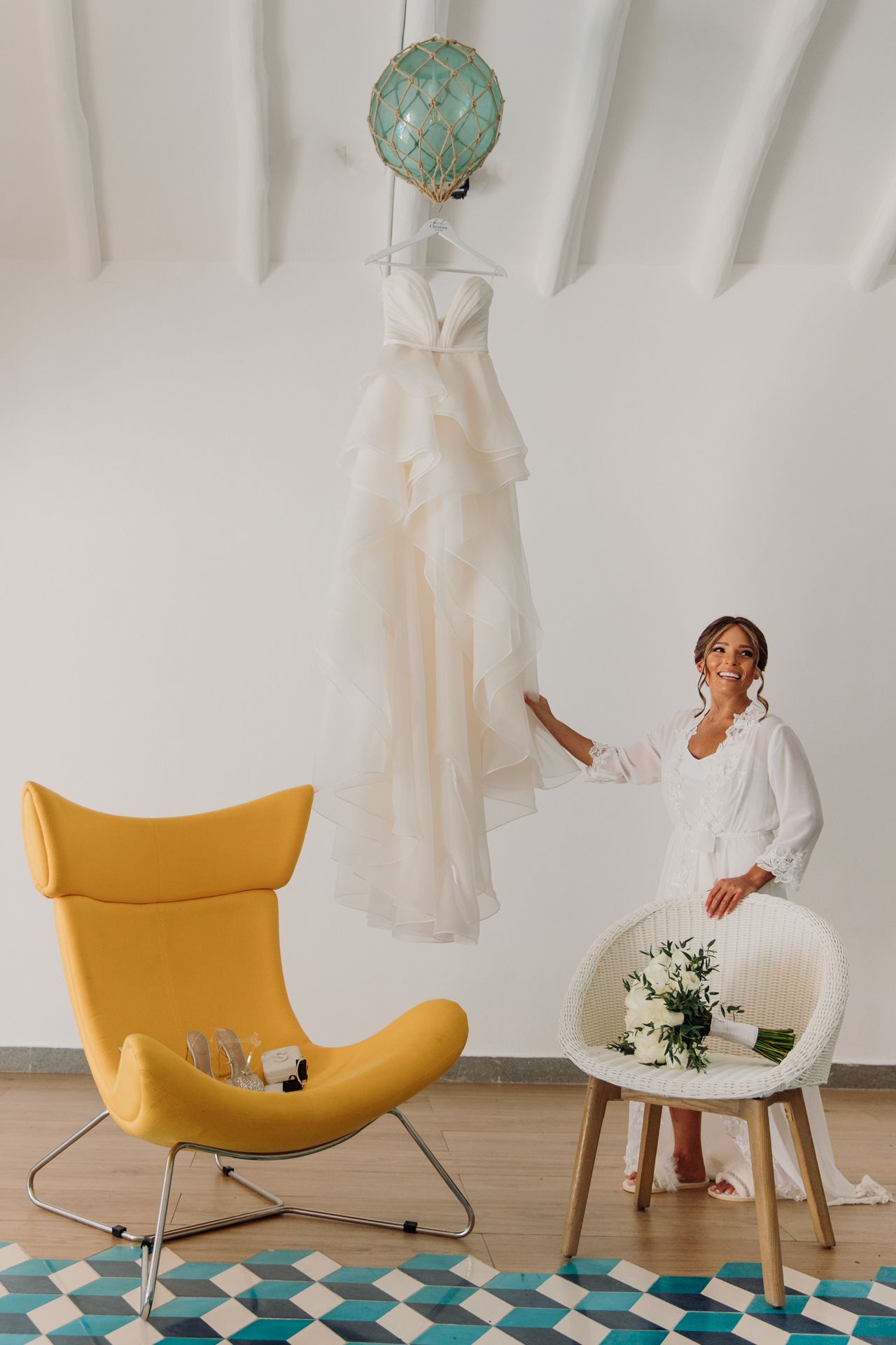 Wedding dress hanging from turquoise balloon with yellow chair and geometric rug in minimal white room setting. El Dorado Royale Wedding