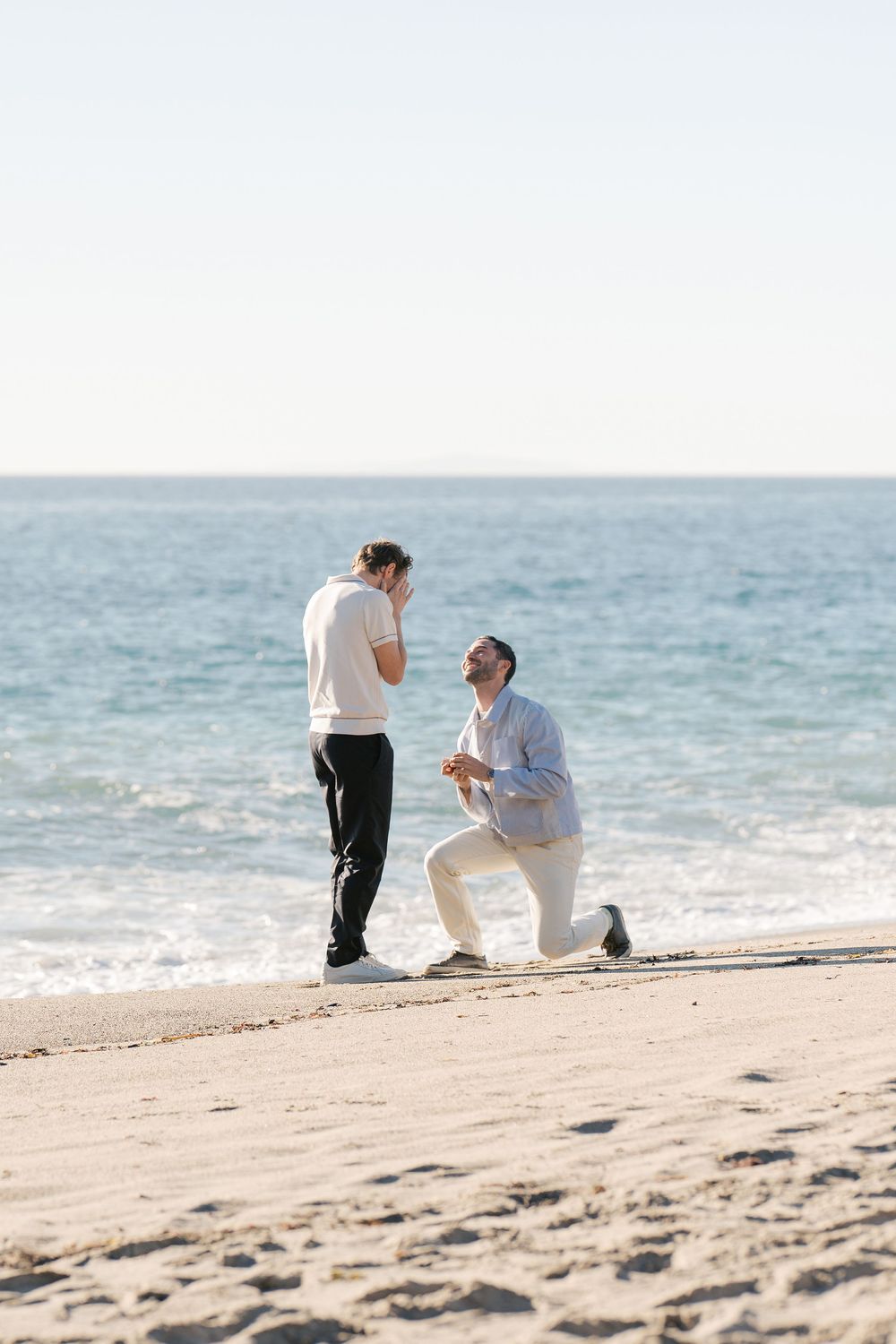 A romantic beach proposal moment captured during sunset with the ocean as backdrop.