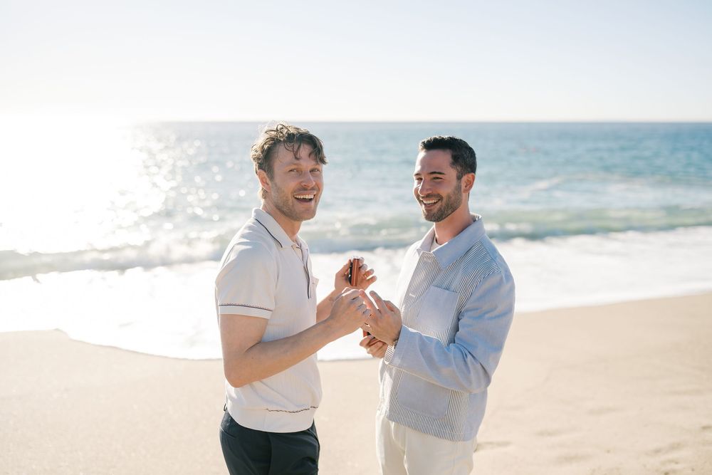 Two people share a romantic moment together while standing on a sunny beach with ocean waves in the background.