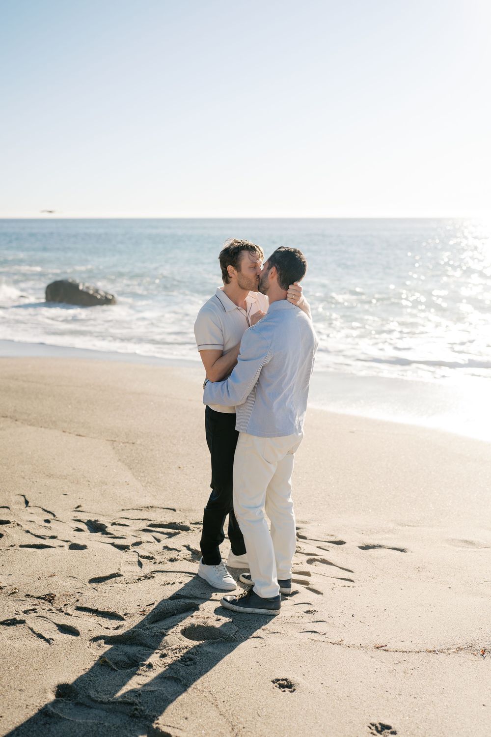 A tender moment shared between two people embracing on a sunlit beach with waves in the background.