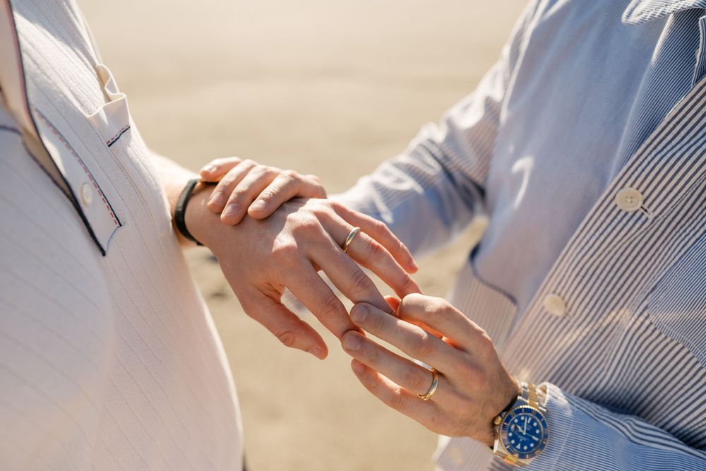 Close-up shot of hands exchanging an engagement ring on a sandy beach.