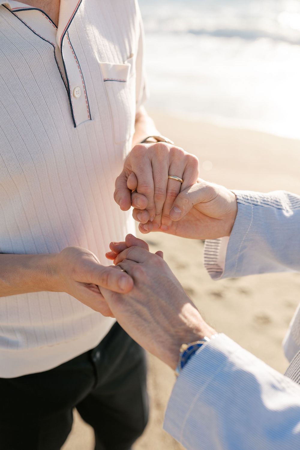 Close-up shot of hands exchanging rings during a beach ceremony at sunset.