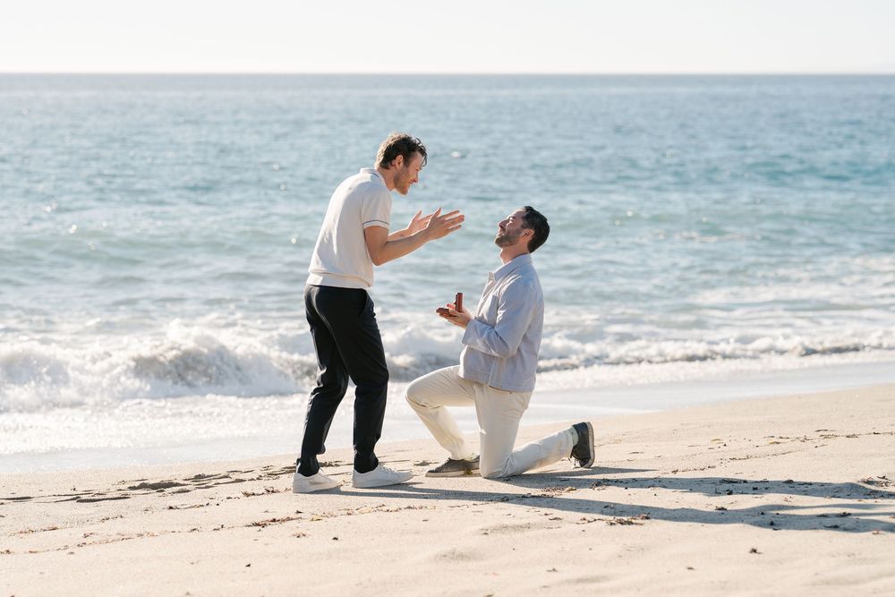 A romantic beach proposal scene with waves crashing in the background at sunset.