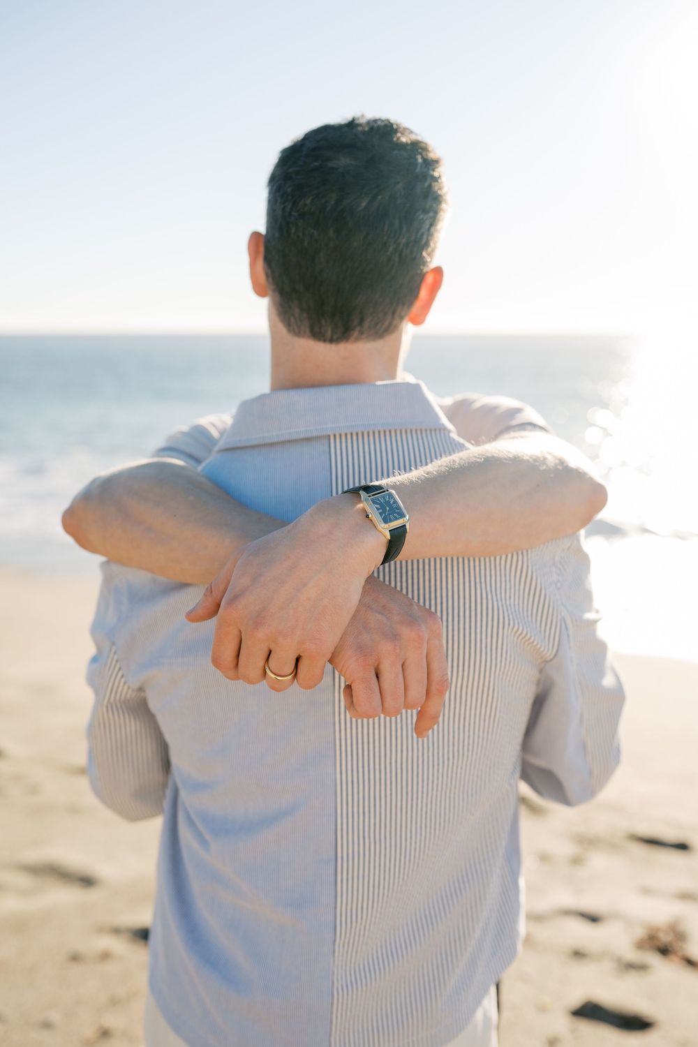 Back view of someone wearing a striped shirt showing their wedding ring on a beach at sunset.