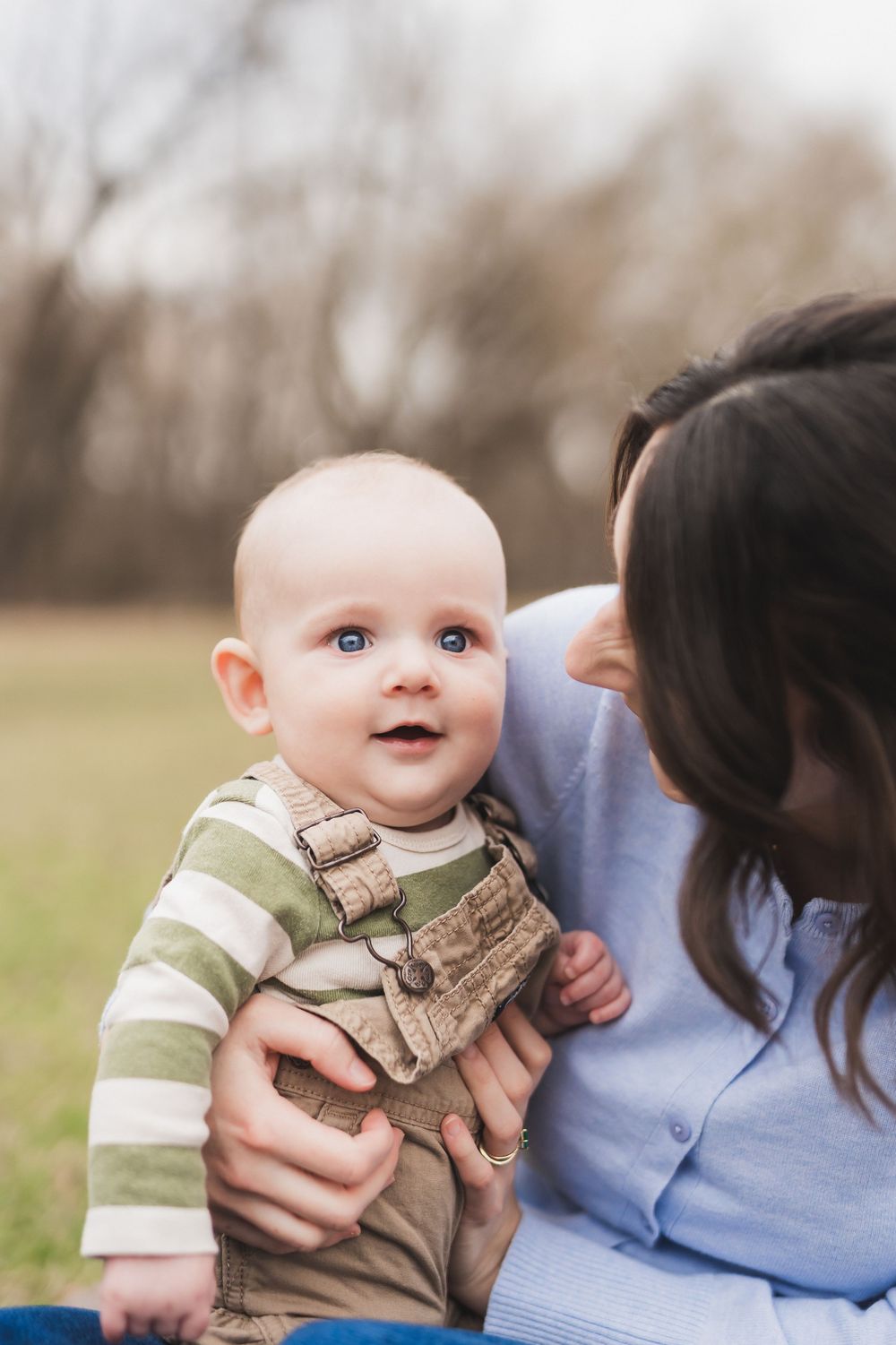 A tender moment captured outdoors showing affectionate interaction with a baby wearing a camouflage outfit.