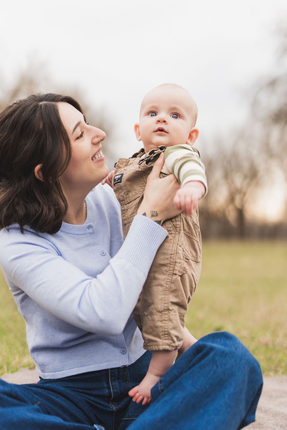 A tender outdoor moment between parent and baby wearing brown and blue on a sunny afternoon.
