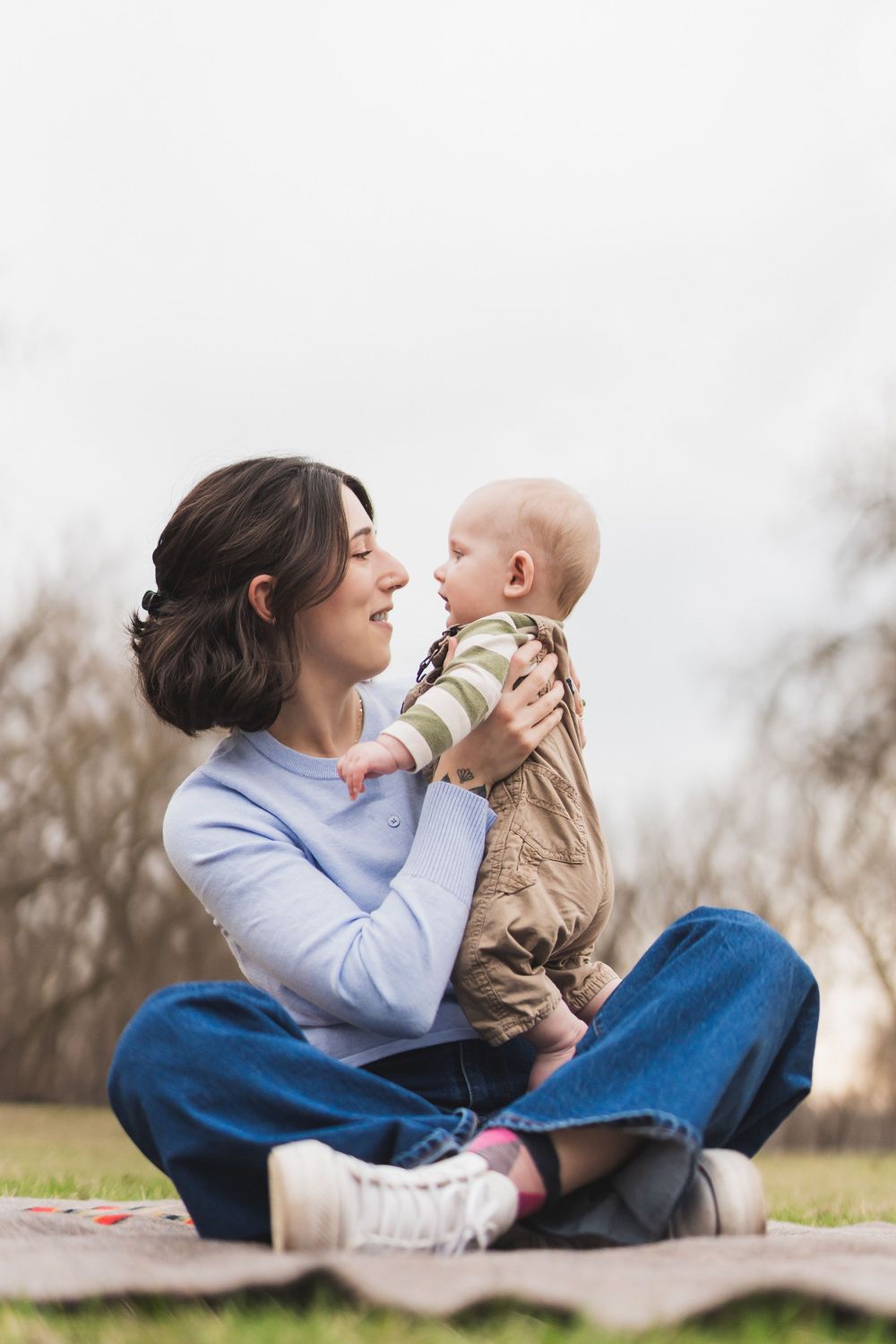 A tender moment captured outdoors showing affection between parent and baby while lying on grass.