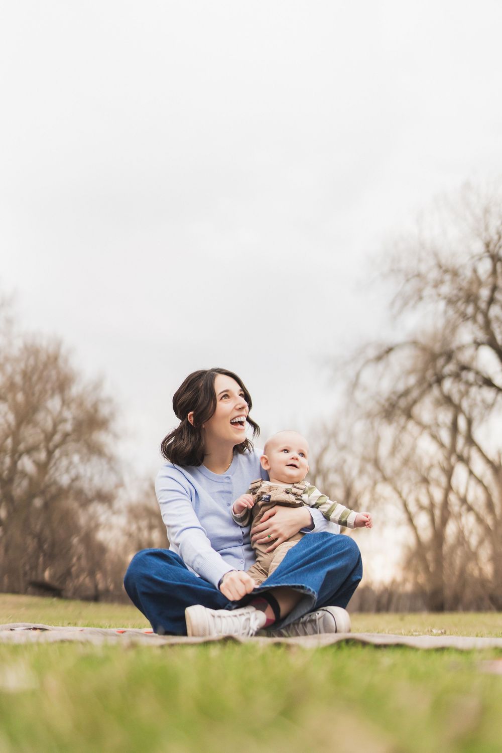 Parent and baby share joyful moments together while relaxing on grass in a natural outdoor setting.