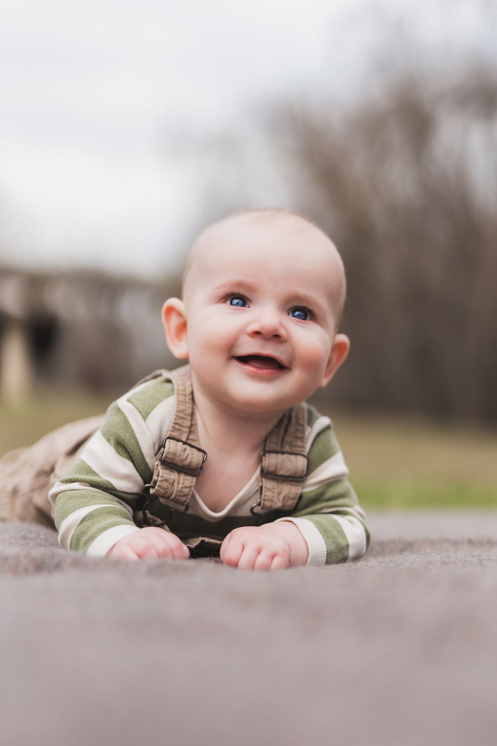 Baby in striped outfit lying on stone surface while looking up with bright blue eyes and sweet smile.