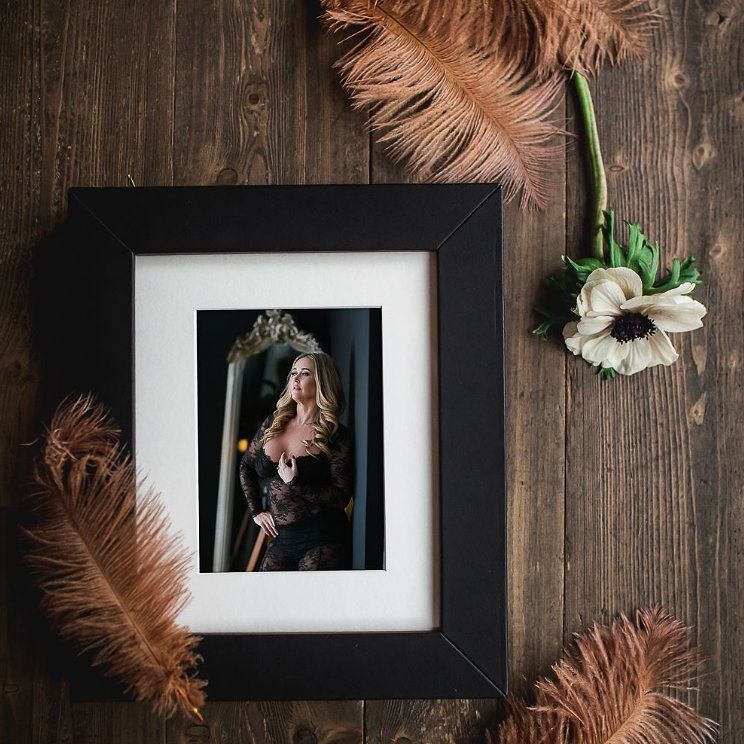 Artistic arrangement of pink feathers and floral elements against a rustic wooden backdrop with a matted, framed photograph.