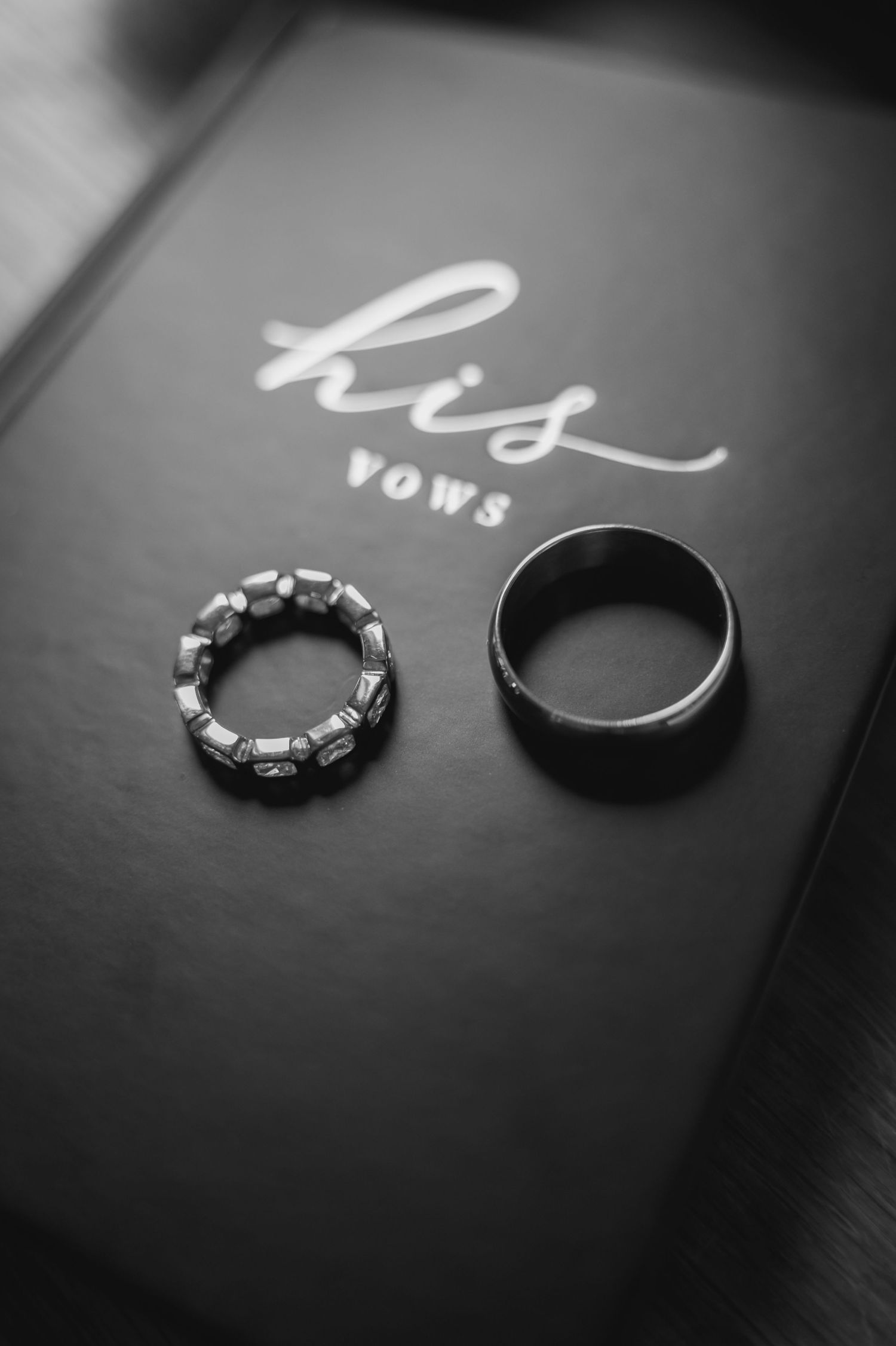 Wedding rings and vows book displayed on dark surface with elegant calligraphy details.