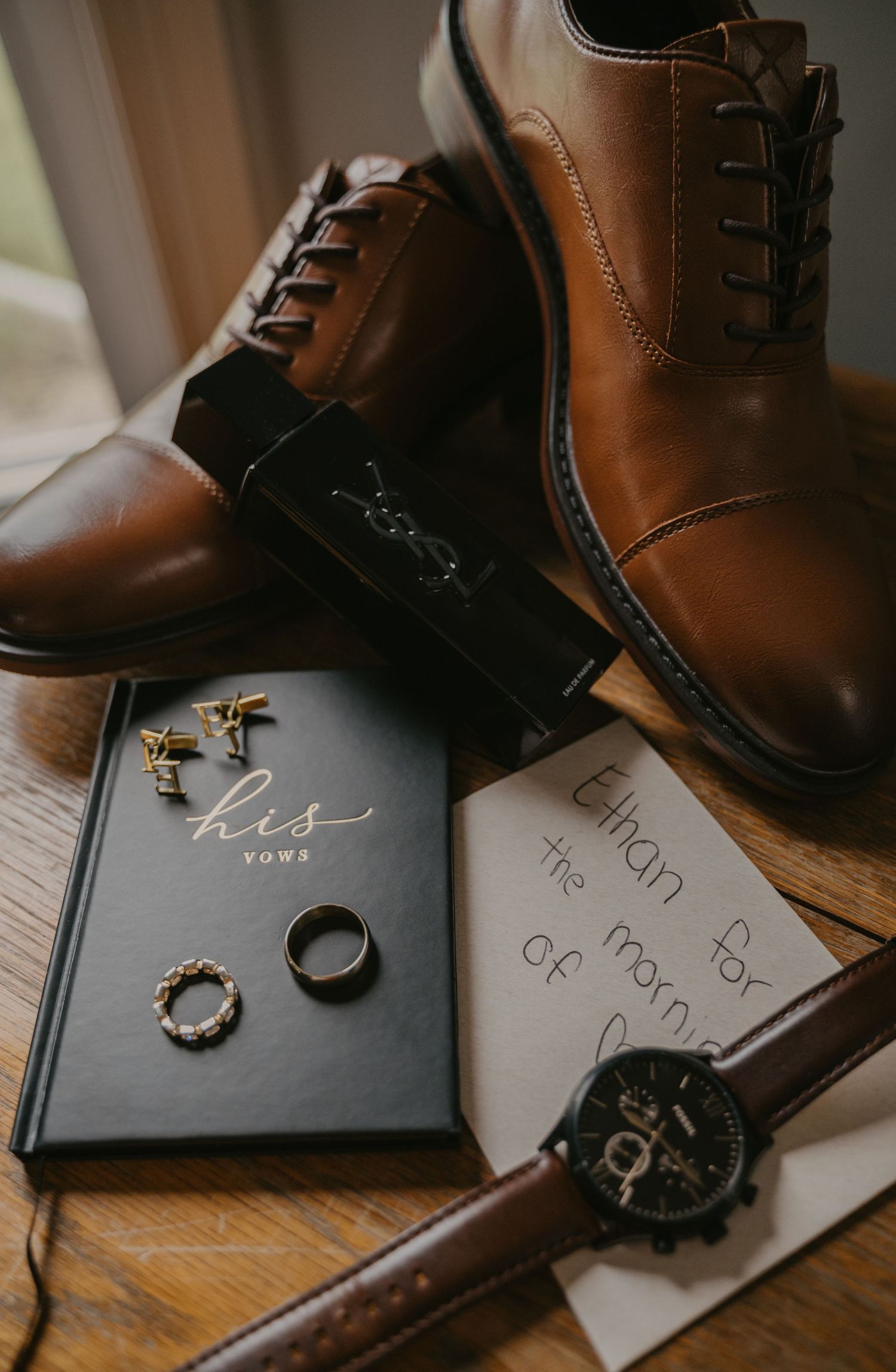 Brown leather dress shoes and wedding rings displayed on handwritten vows against a wooden surface.