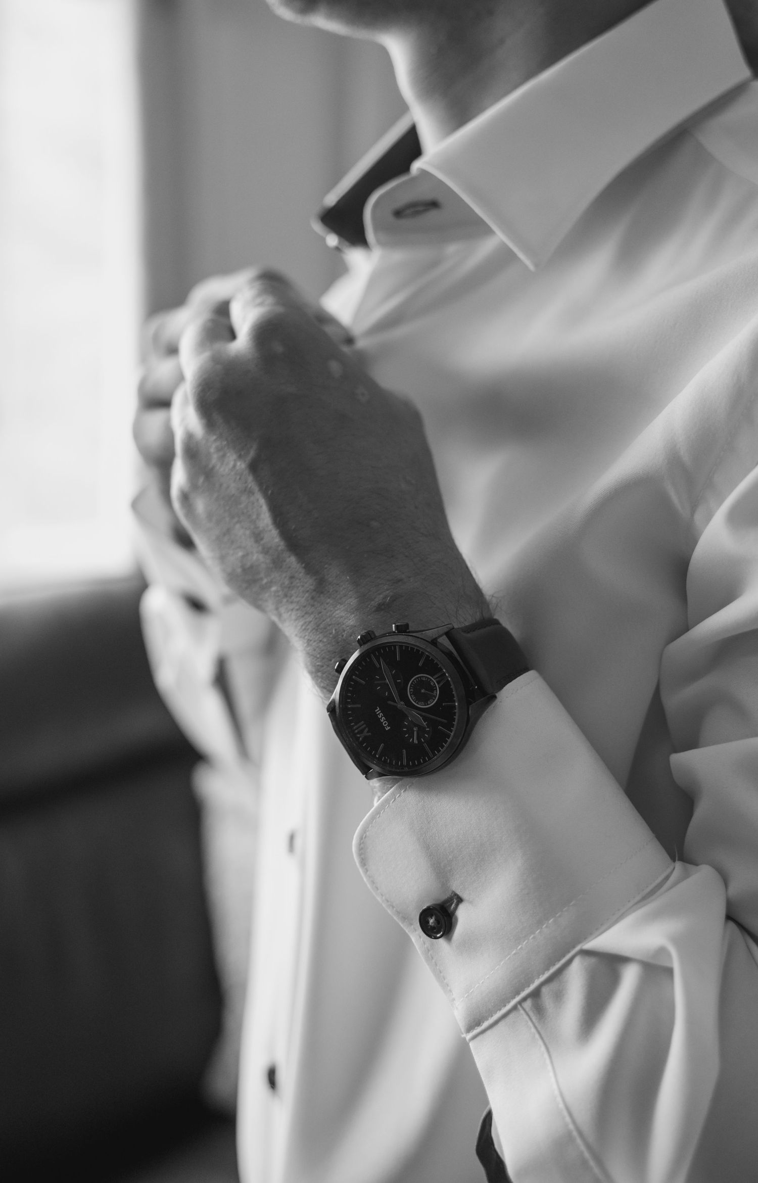 Close-up black and white detail of a wristwatch against a white sleeve.