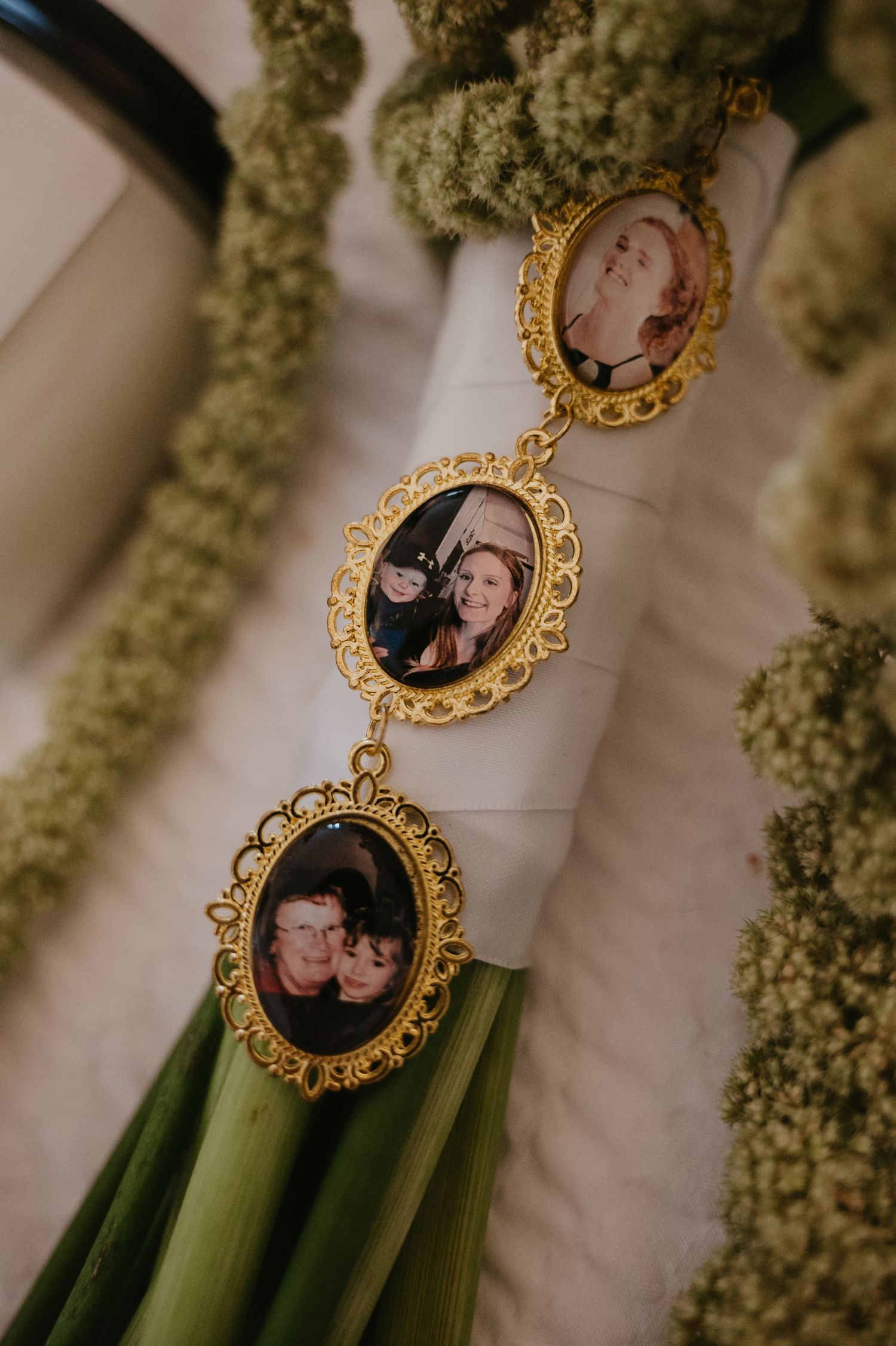Ornate gold-framed photo charms with vintage portraits hang against a backdrop of green foliage.
