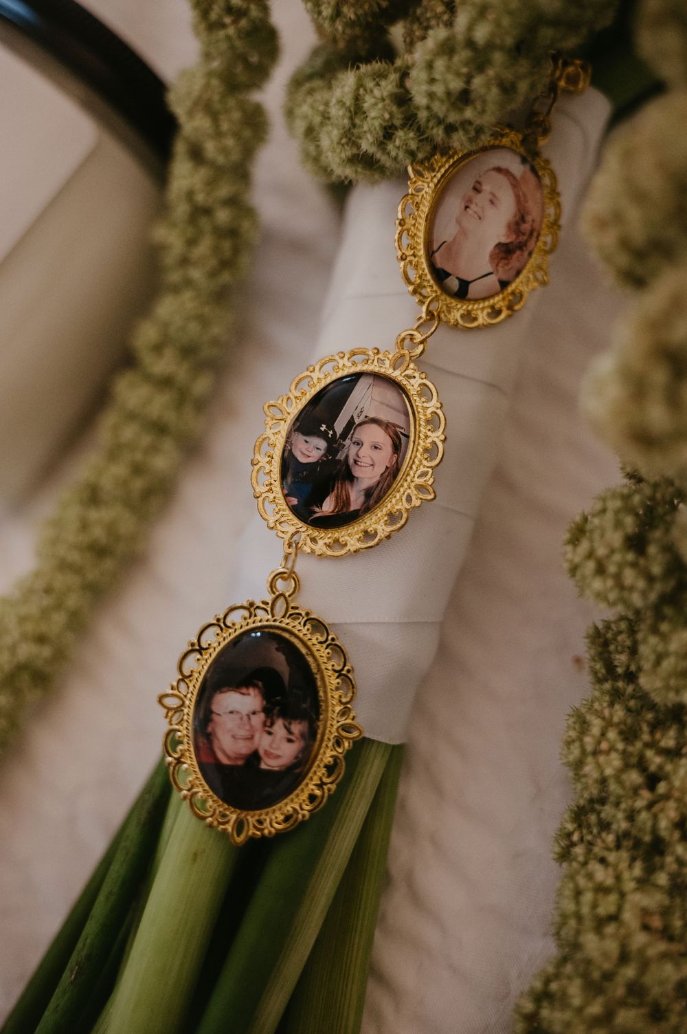 Ornate gold-framed photo charms with vintage portraits hang against a backdrop of green foliage.