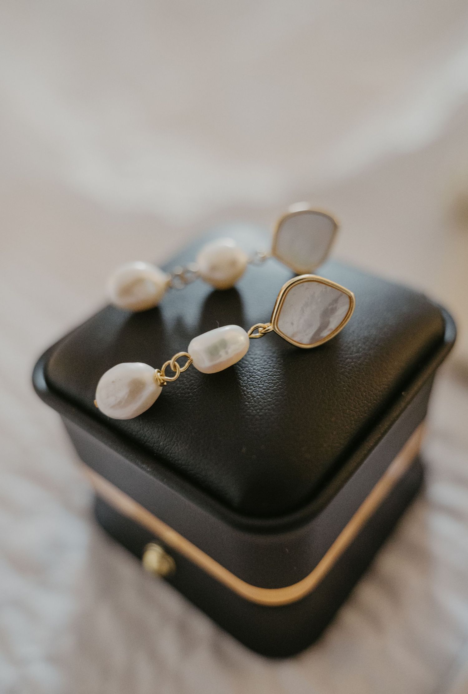 Elegant pearl drop earrings with gold settings rest on a black leather jewelry box with metallic trim.