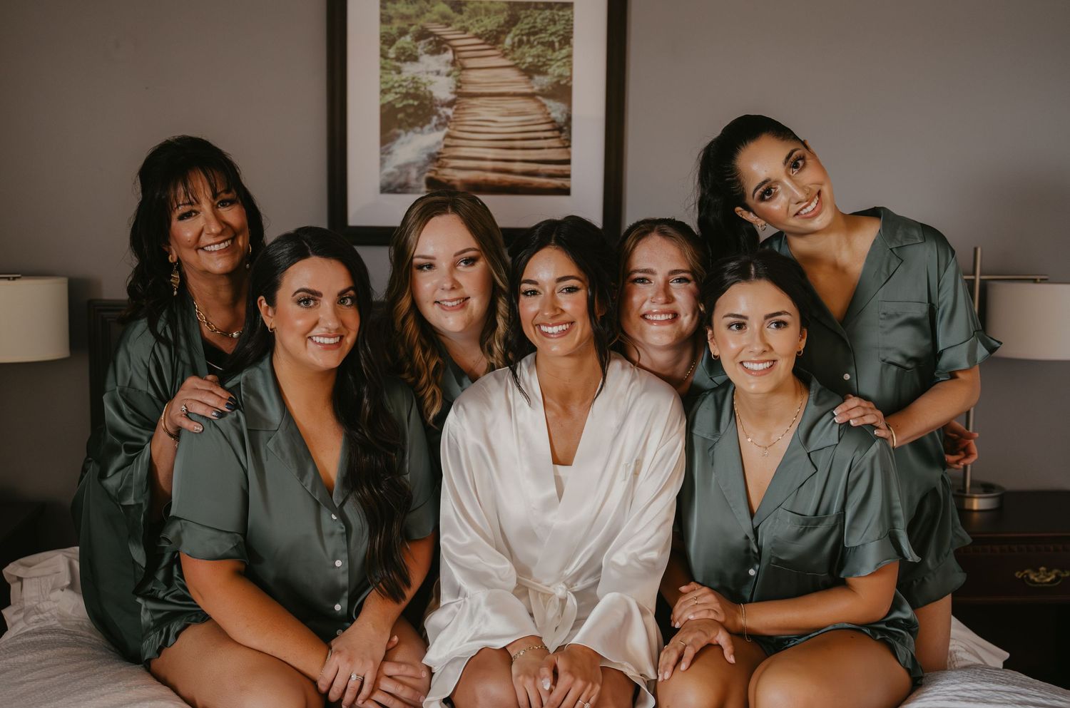 A group of bridesmaids in matching gray robes gather together for pre-wedding photos in a room.
