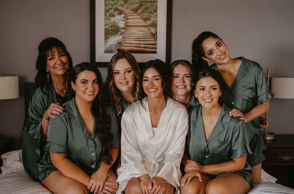 A group of bridesmaids in matching gray robes gather together for pre-wedding photos in a room.