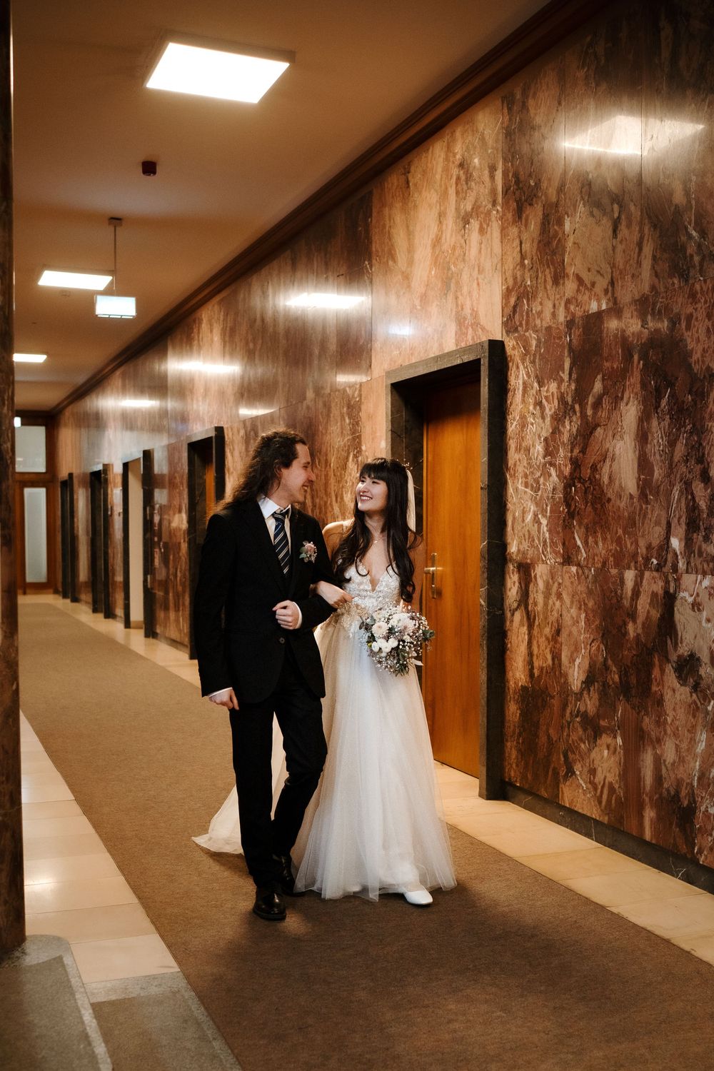 A bride and groom share a romantic moment in a rustic hallway with textured brown walls and warm lighting.