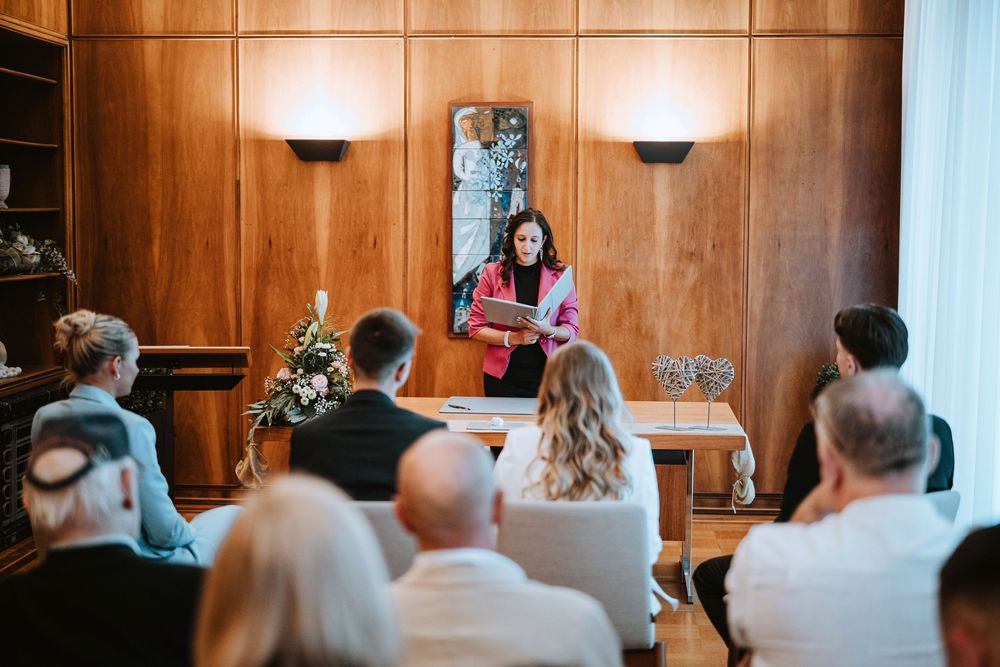 Wedding ceremony taking place in a wood-paneled room with guests seated in rows watching the proceedings.