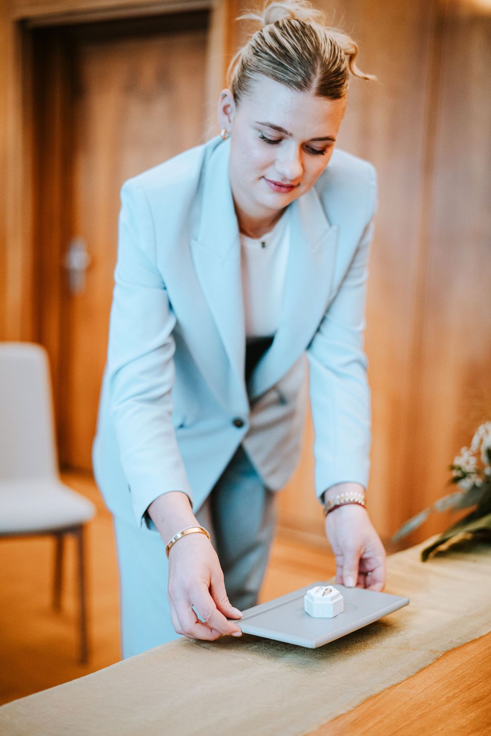 Professional in light blue blazer arranging items on wooden table in office setting.