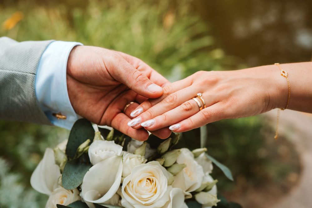 A close-up view of hands exchanging wedding rings during an outdoor ceremony with white roses in the background.