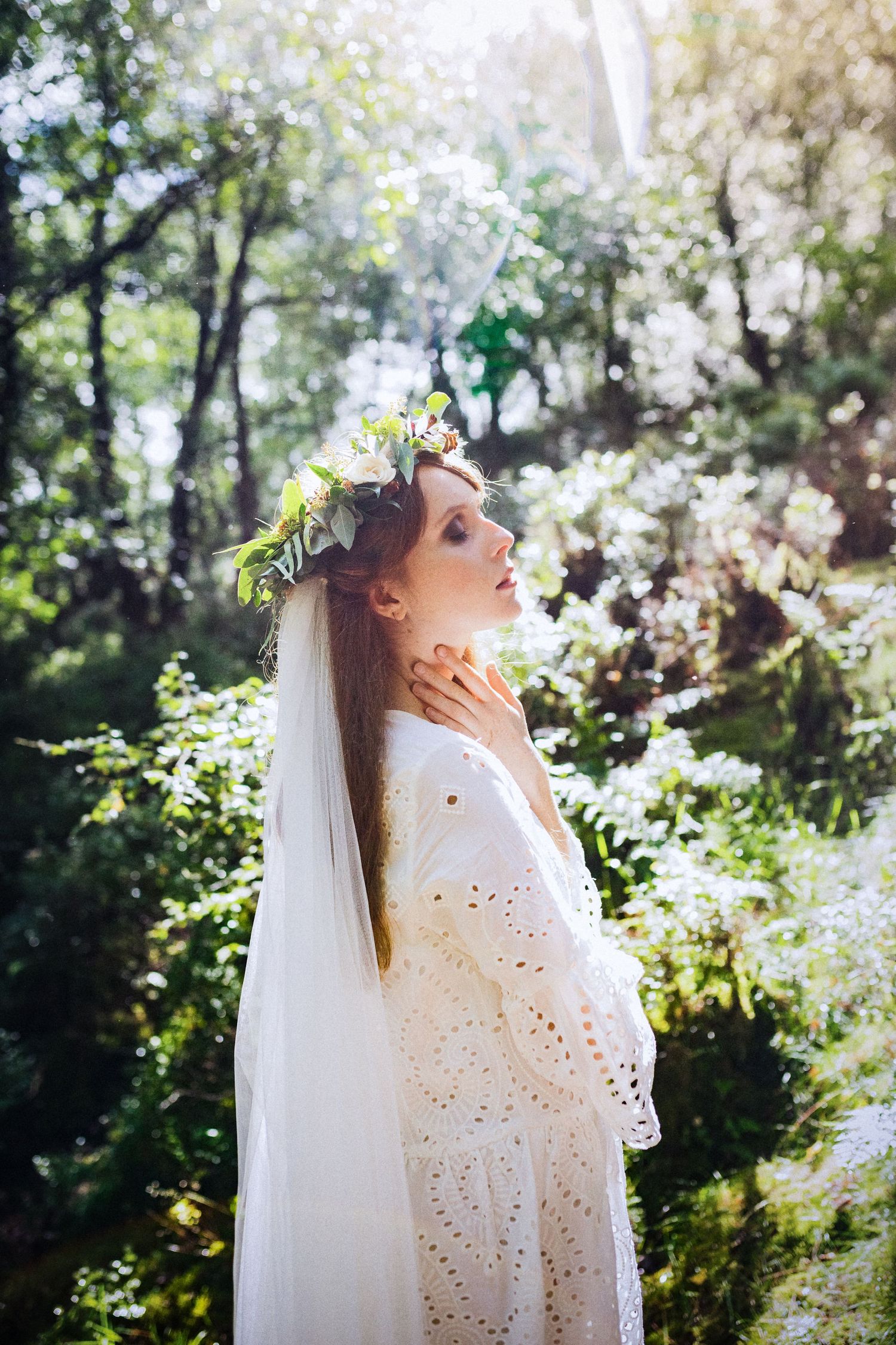 Ethereal bridal portrait with floral crown in dappled sunlight through trees.