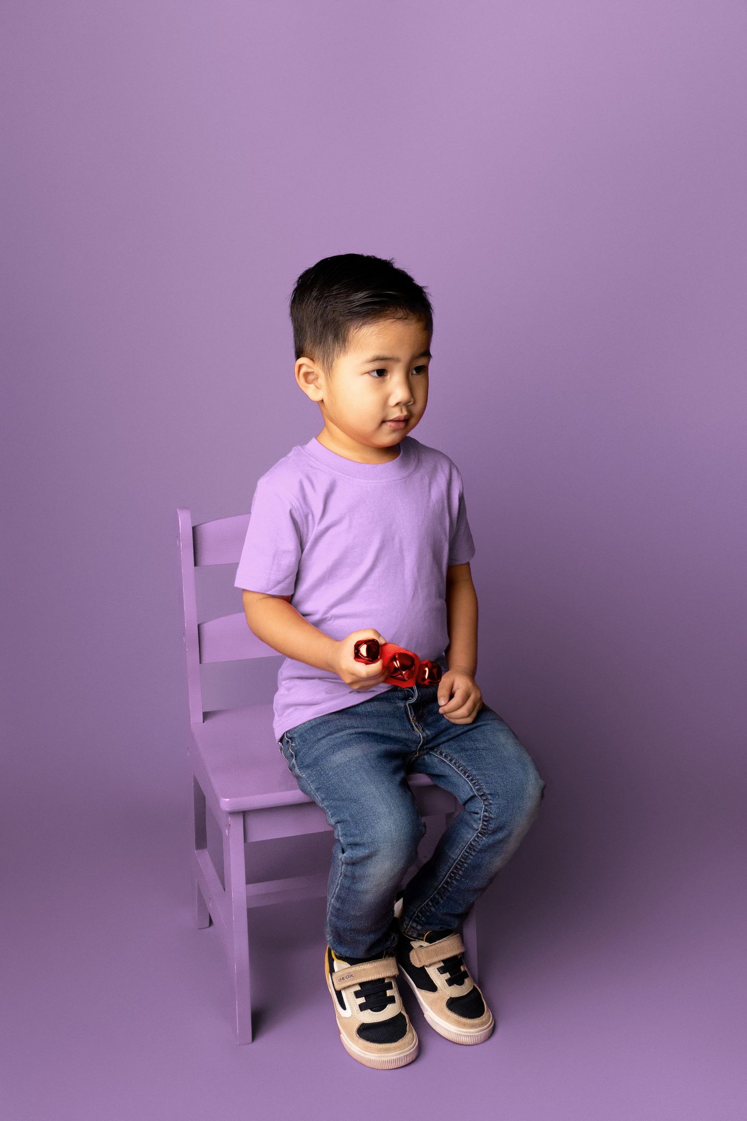 Studio portraits on a purple chair wearing casual attire against a lilac background.