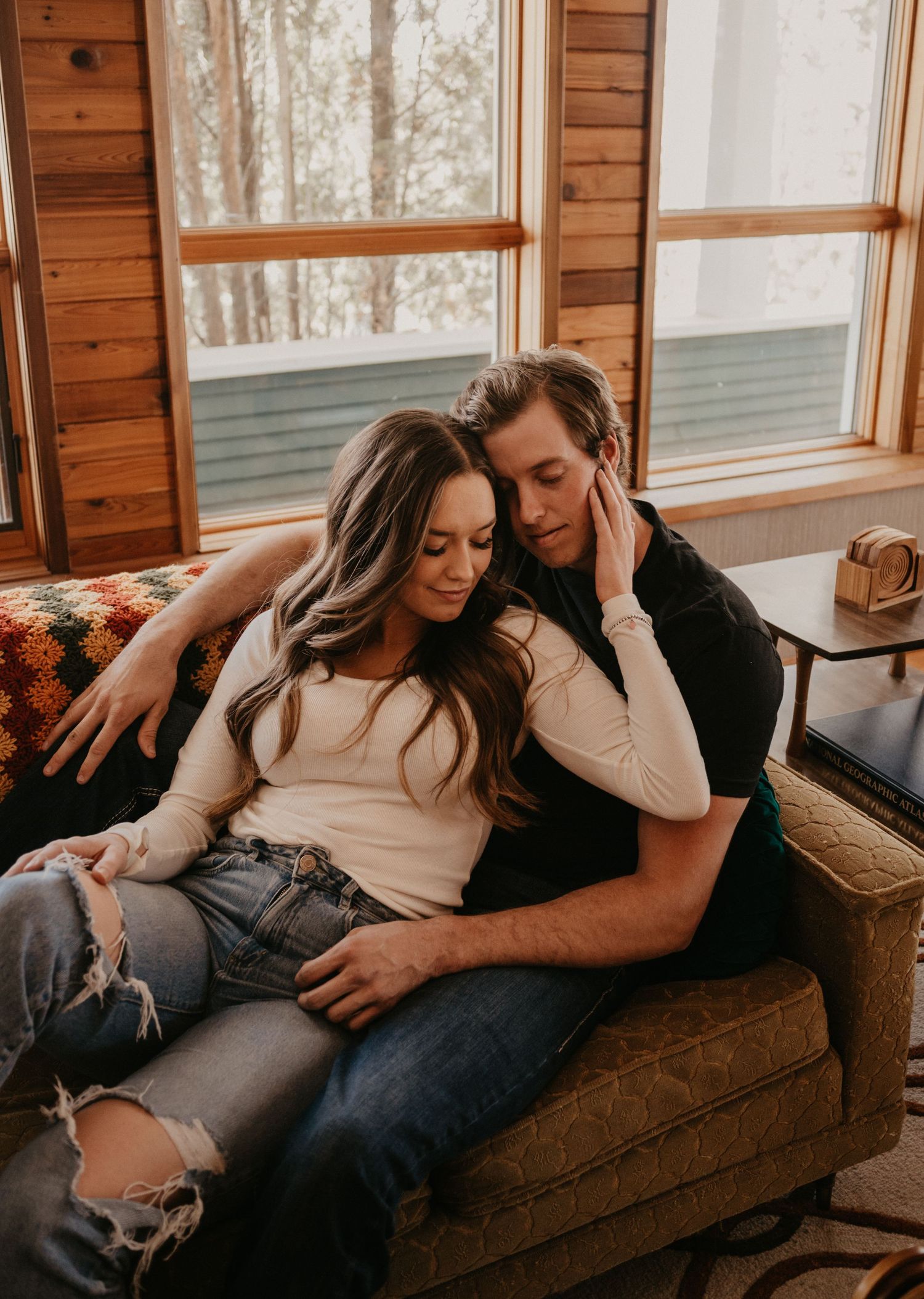 A couple shares an intimate moment while relaxing together on a brown couch in a rustic cabin setting.
