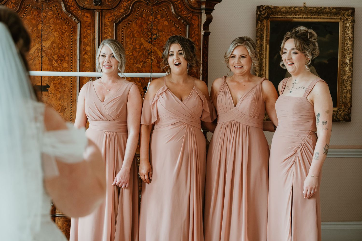 Bridesmaids in matching blush pink wrap dresses stand together in an elegant indoor setting.