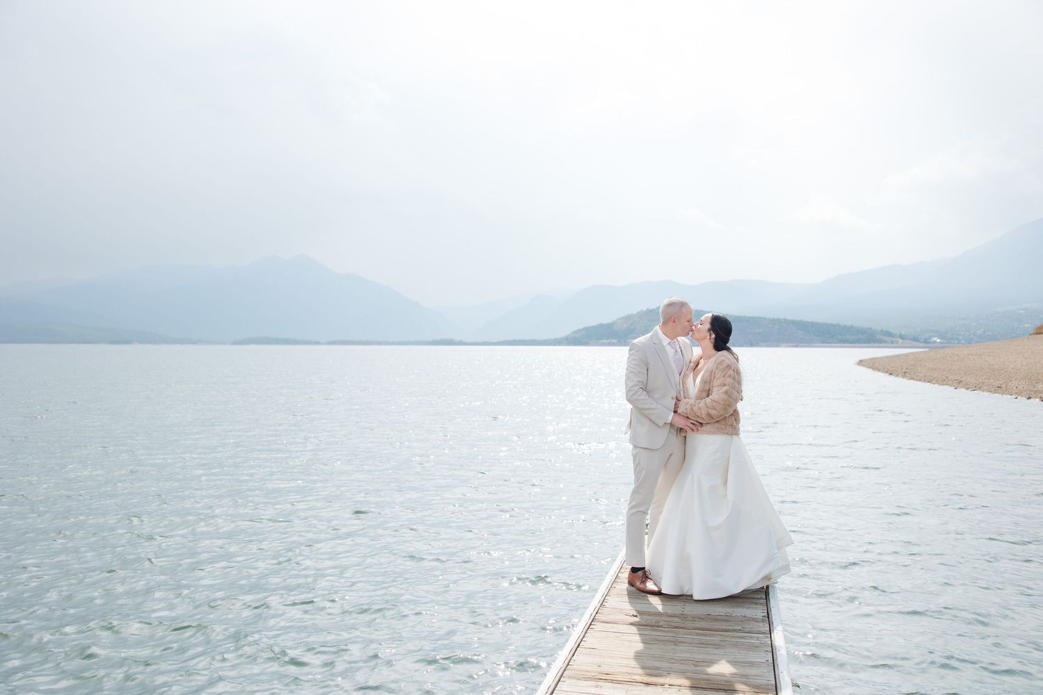 A couple in light colored attire shares a romantic moment on a bright sandy beach.