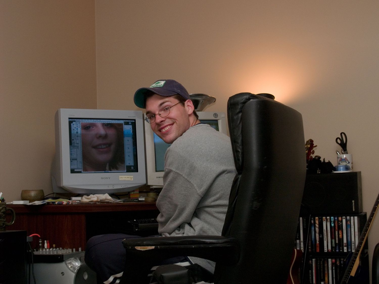 Person in black hoodie sitting at home studio setup with keyboard and music equipment in black and white photo.