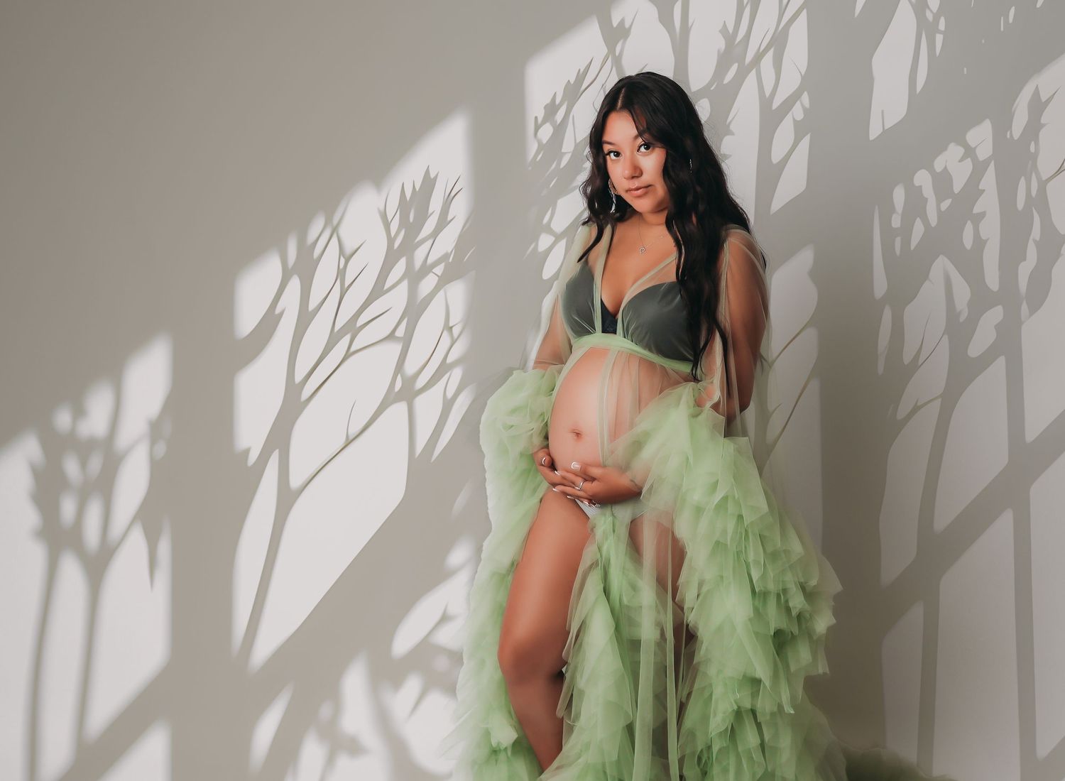 Woman in green tulle dress poses against wall with dramatic tree shadow patterns.
