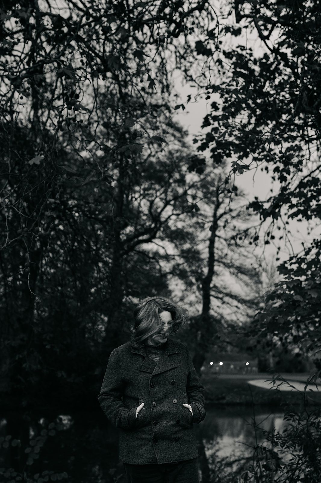 Vintage black and white photo showing people sitting on a bench in a park surrounded by trees and foliage.