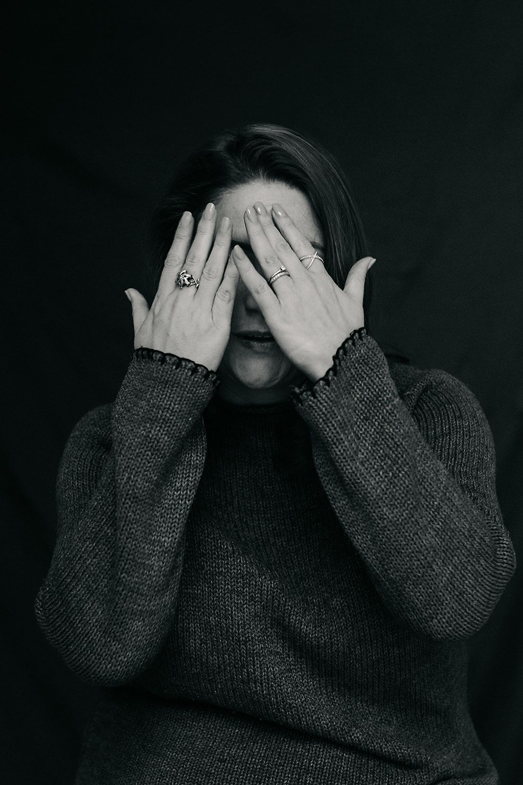 Person in dark gray sweater covers their face with both hands in a series of moody, dark photographs. Author headshots london