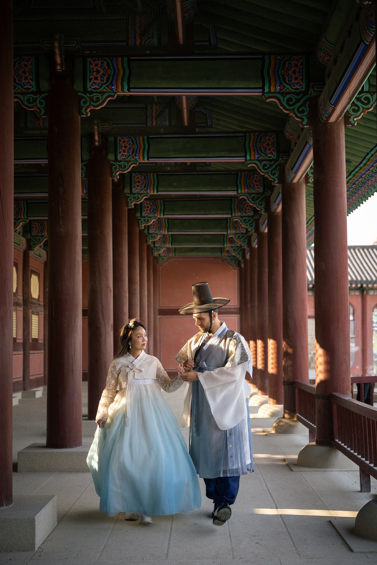 People in traditional Korean hanbok attire walk through a covered wooden walkway at Gyeongbokgung Palace in Seoul.